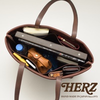 深棕色皮革極簡托特包，內部裝有書本、皮夾、水瓶、手機等物品，包包內有分隔層，展現其容量與收納功能。