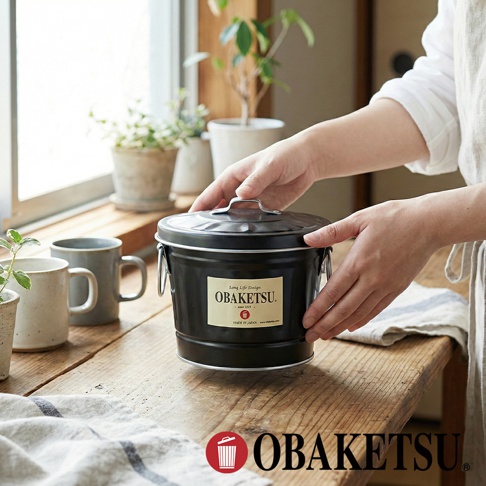 OBKETSU 手工製迷你桶，黑色鍍鋅鋼材質，附有品牌標籤，展示於木桌上，背景為窗戶與綠植