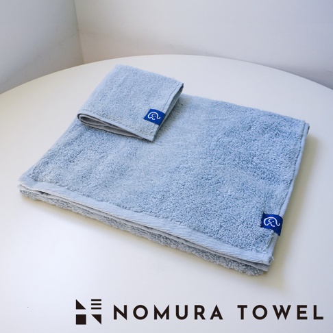 淺藍色方巾和毛巾，帶有藍色小象圖標的織標，以及「NOMURA TOWEL」字樣。