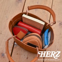 職人手作皮革三角飯糰造型小物收納包，顏色為棕色，包內裝有紅色小錢包、褐色小錢包、書籍和濕紙巾。