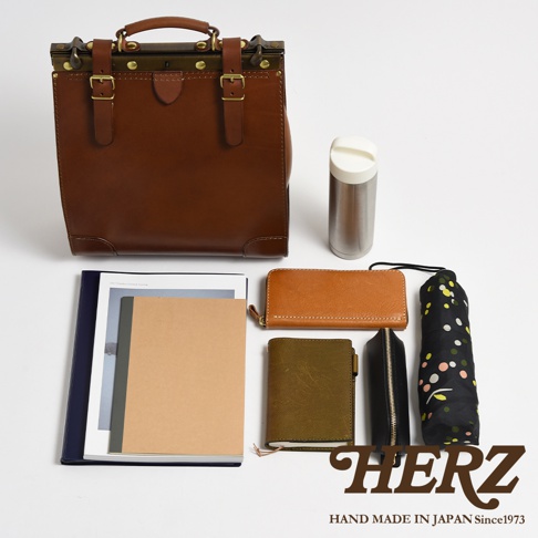 職人手作皮革復古口金後背包，主體為棕色皮革，搭配黃銅色五金配件，另有筆記本、長夾、小錢包、保溫瓶及印花摺疊傘。