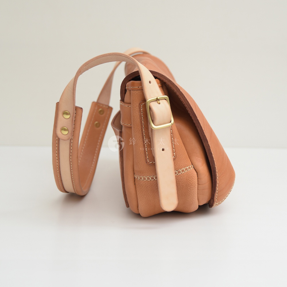 職人手作皮革郵差包，淺棕色皮革，側面帶有縫線細節，可調節的皮革肩帶，搭配金色金屬扣環。