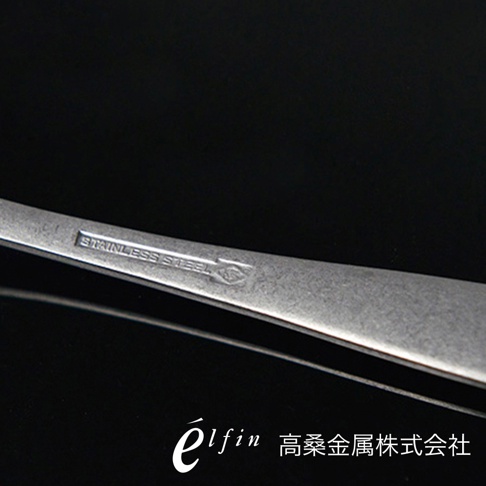 日製熔岩黑石餐匙，金屬材質，表面有「STAINLESS STEEL」字樣及品牌標誌。