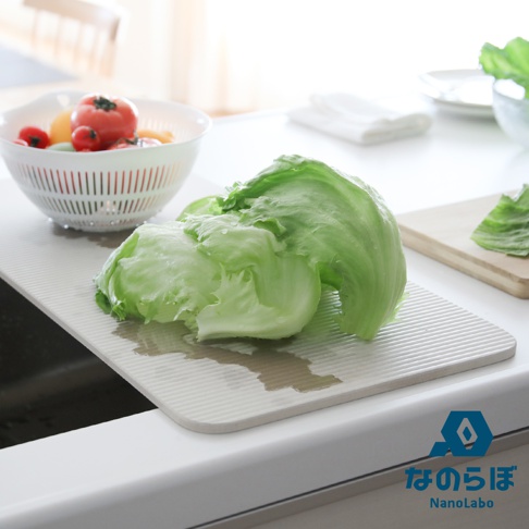 淺灰色條紋珪藻土置物墊上放著兩顆結實的綠色結球萵苣，旁邊有一個白色濾水籃，籃內裝有番茄、小番茄和黃色蔬菜。