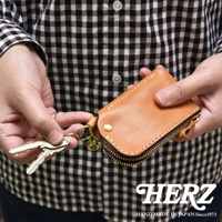 職人手作皮革鑰匙包，採用天然皮革材質，呈現自然的棕褐色，設有拉鍊開合及金屬掛鉤，可收納鑰匙，設計簡約實用。