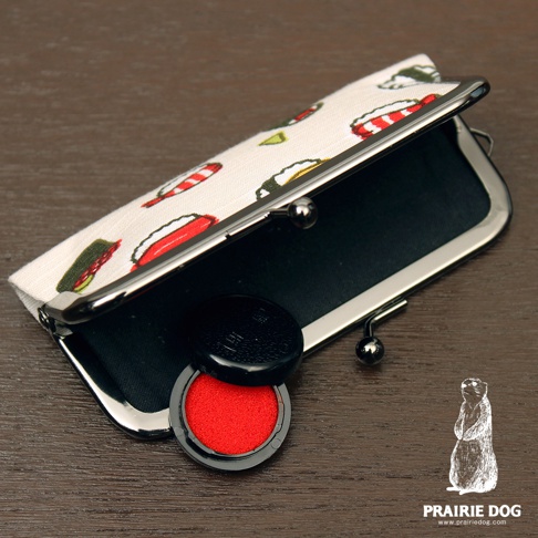 一個印有和布華圖案的口金包，內有黑色內襯。旁邊擺放著一個紅色印泥和黑色蓋子。