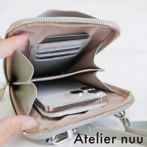 Atelier nuu 手機包打開後的特寫視角，內側淺灰色皮革夾層設有多個信用卡卡槽，主袋空間放入一支白色智慧型手機，整體設計簡約實用，呈現出精緻的皮革質感。