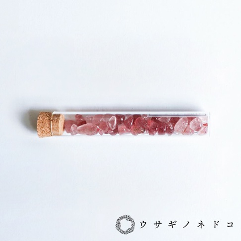 玻璃試管內裝有數顆粉紅色或淡紅色、不規則形狀的礦石碎片，試管口以軟木塞封緊，背景為純白色。