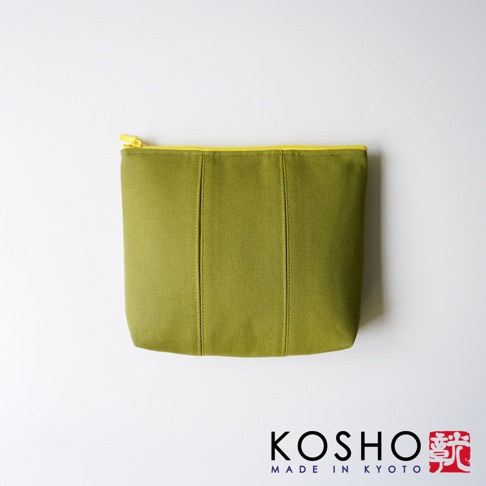 京都KOSHO帆布化妝收納包，呈現橄欖綠色調，外觀為簡約素雅的帆布材質，表面帶有細緻紋理與兩條垂直拼接線設計，搭配鮮明亮眼的黃色拉鍊，整體採用俯視視角拍攝，品牌LOGO與MADE IN KYOTO字樣位於右下角。