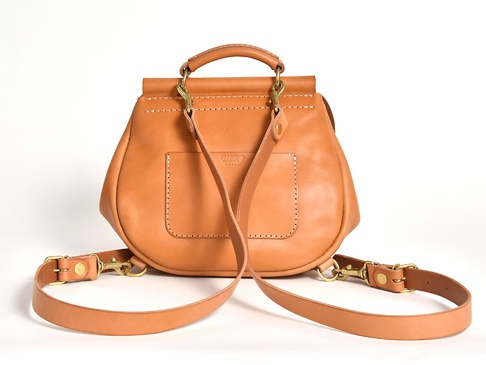 天然皮革製成的迷你後背包，呈現自然棕色，帶有手提把和可拆卸肩帶，以黃銅金屬扣件固定，包身後方有縫線裝飾的方形口袋。