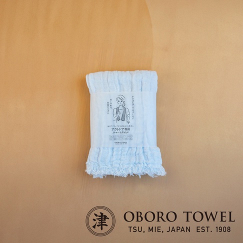 淡藍色三層紗純棉掛脖毛巾，帶有細緻的流蘇邊緣，包裝上印有女性運動圖案與日文說明。