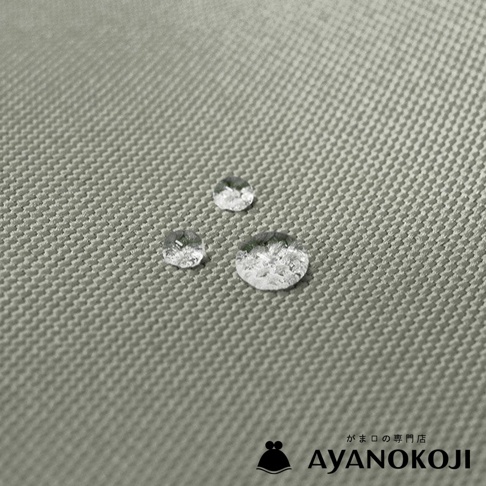 圖片內文字「がま口の専門店 AYANOKOJI」，與三個水滴在淺灰綠色布料上，展現布料的防水特性。