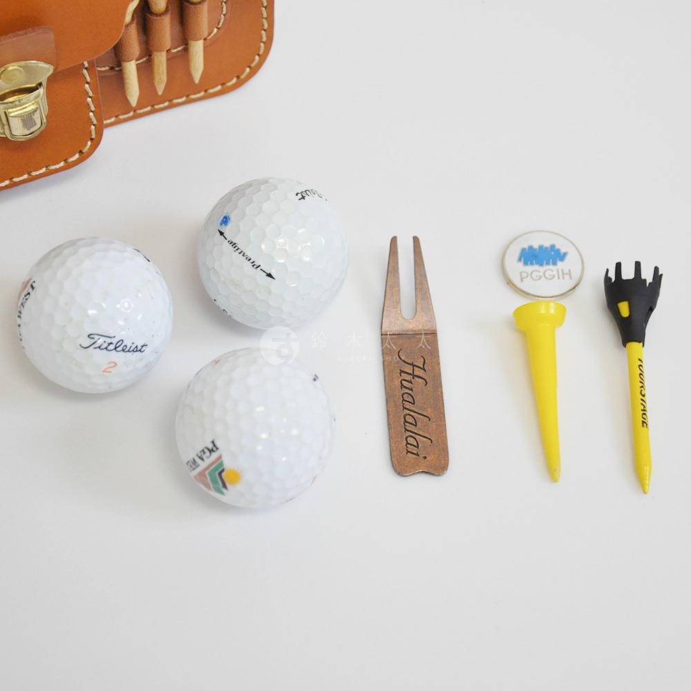 職人手作皮革高爾夫腰包 E-81 的配件，包含三個白色高爾夫球、一個銅色高爾夫球叉、一個圓形標記、一個黃色高爾夫球座及一個黑色高爾夫球座。