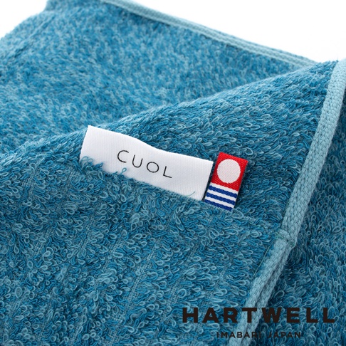 藍色紋理毛巾，質地柔軟，有「CUOL」品牌標籤和帶有圓點與條紋的裝飾標籤。