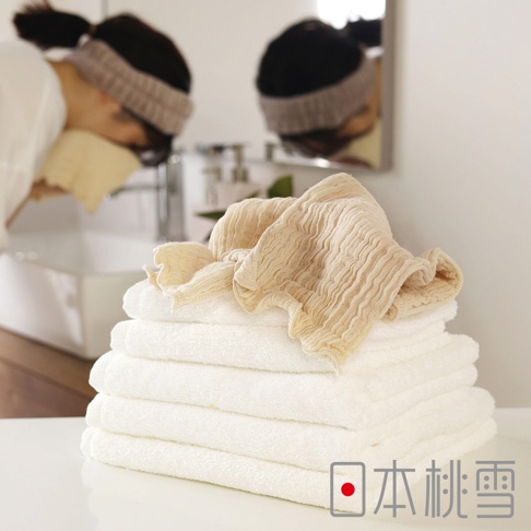 堆疊的白色毛巾上放著一條米黃色褶皺紗布毛巾，背景是正在洗臉的女士和鏡子裡的倒影。