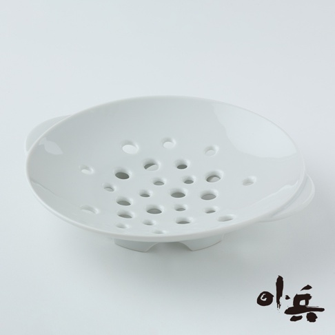 白色陶瓷美濃燒多用蒸盤，盤面佈滿大小不一的圓孔，盤底有三個支撐腳，兩側有提把，造型簡潔。