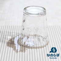 一個帶有圓形紋飾的透明玻璃杯倒置在條紋狀的珪藻土吸水墊上，杯底周圍有水漬。