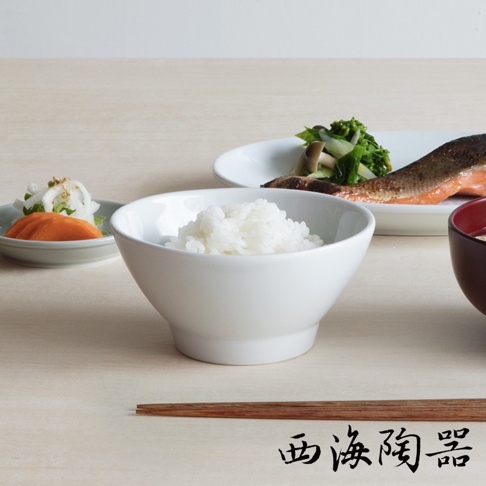 白色陶瓷飯碗裝有飽滿的白米飯，旁邊擺放著鮭魚、蔬菜、醃漬小菜和一碗味噌湯。