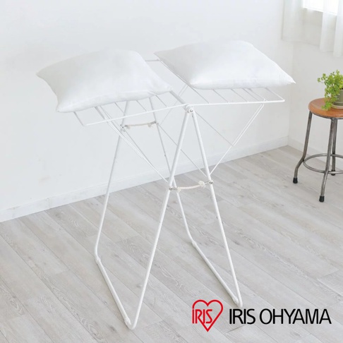 白色金屬蝴蝶式曬衣架，展開狀態，上方放置兩個白色枕頭。曬衣架結構簡潔，由多條白色金屬桿組成，以「X」形支撐。