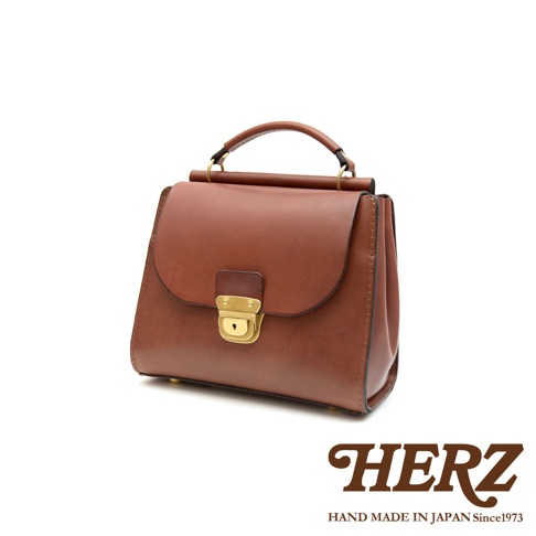 HERZ 職人手作皮革屋瓦風兩用單肩包，棕色硬皮革材質，配有復古金色鎖扣和提把。