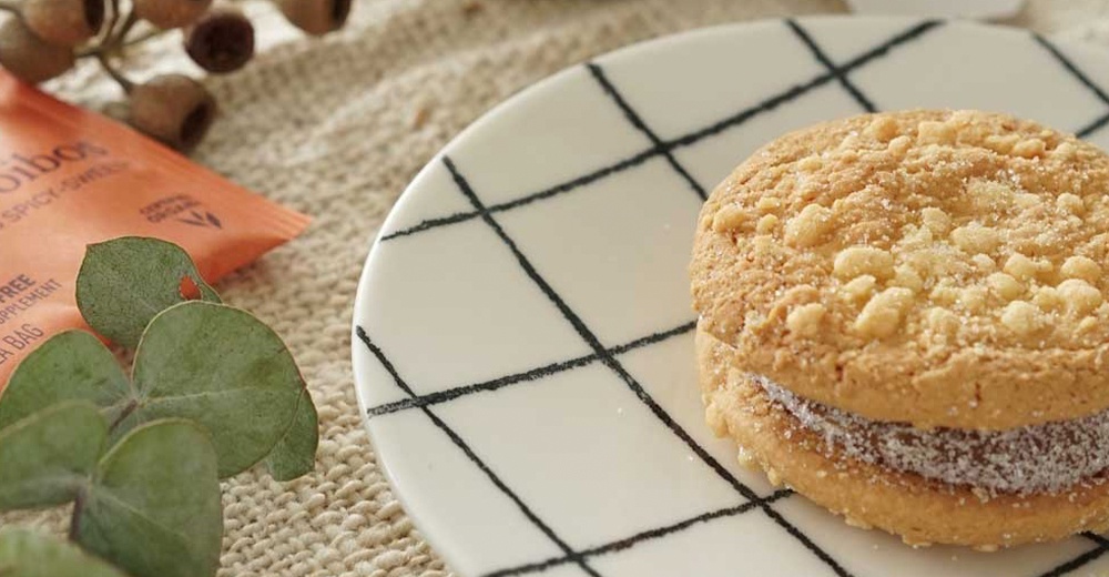 美濃燒手繪點心盤，白色盤面飾有黑色線條網格，盤上放著一個夾心餅乾，餅乾頂部撒有碎粒和糖粉。