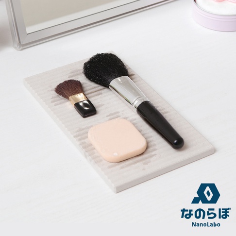 淺灰色條紋珪藻土置物墊上，放置著一支黑色手柄的大號化妝刷，一支小號化妝刷，以及一個膚色化妝海綿。
