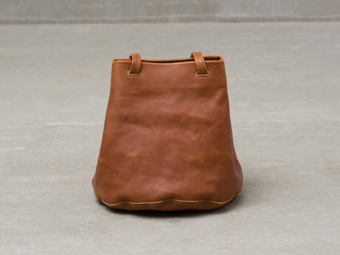 棕色皮革製成的抽繩水桶包，有兩個短提把，底部有波浪邊緣設計。