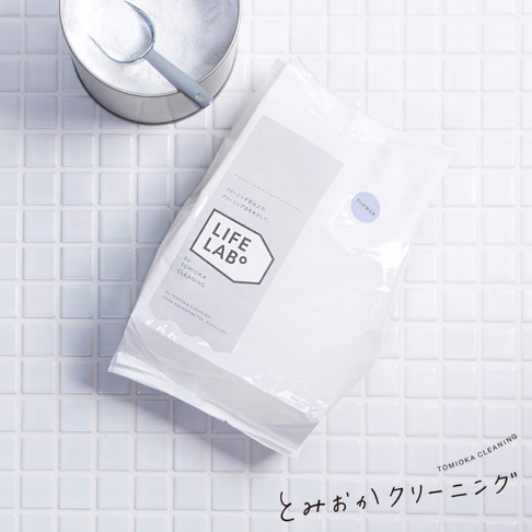 白色補充包裝袋，印有「LIFE LAB」標誌和日文說明，一旁有金屬桶裝白色洗衣粉及灰色勺子，背景為白色小方格磁磚。