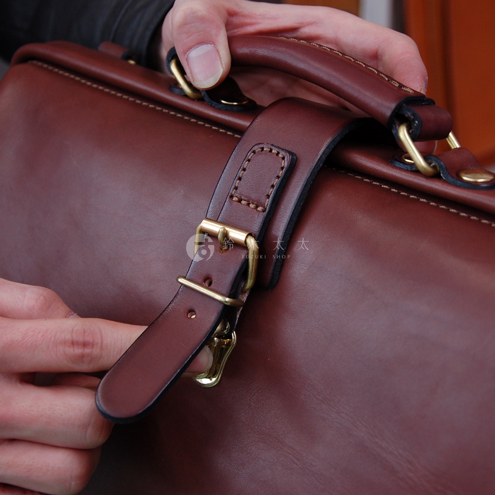 職人手作皮革軟式杜勒斯包，深棕色皮革，配備黃銅扣帶和提把，展現精緻工藝。
