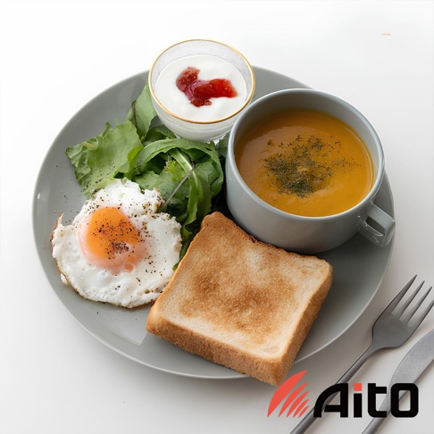 灰色簡約圓形餐盤，盛裝著水煮蛋、烤吐司、南瓜濃湯、優格佐果醬及生菜沙拉，餐盤旁附有餐叉與餐刀。