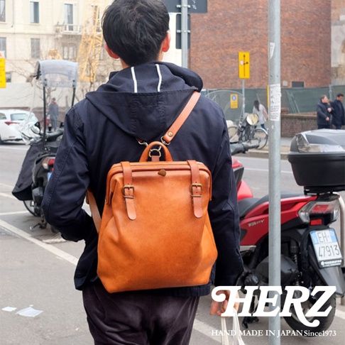 職人手作加厚版皮革後背包 R-143，採用溫暖的棕色皮革，帶有復古風格的搭扣和提把設計，適合日常攜帶。