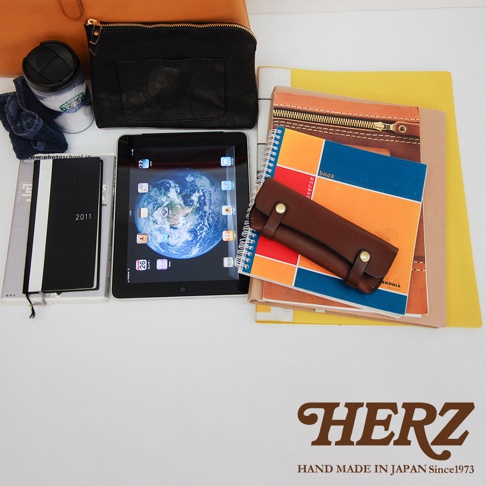 皮革軟式杜勒斯包，黑色，搭配棕色皮革筆套，擺放於筆記本、平板電腦及其他配件上。