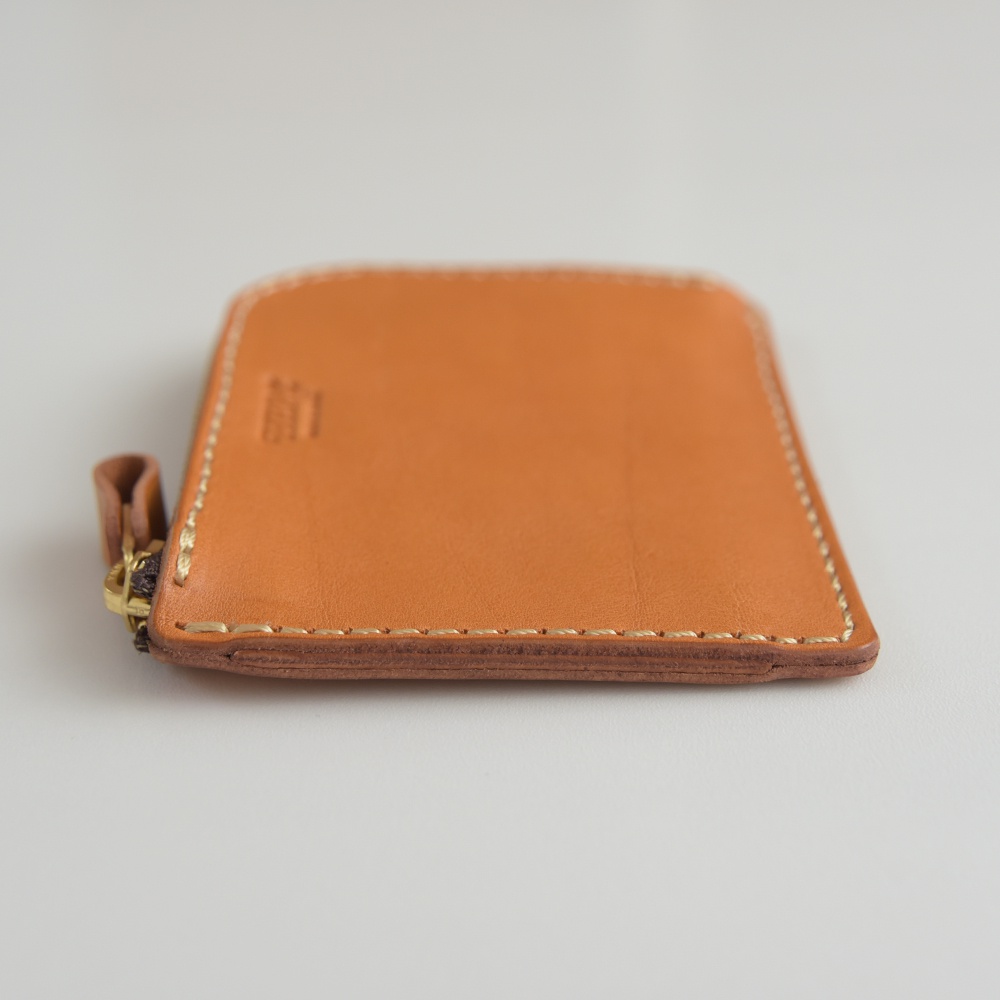 職人手作皮革L型拉鍊迷你短夾，呈現溫潤的橘棕色調，採用真皮材質，車縫線清晰，搭配黃銅色拉鍊與皮革拉頭。