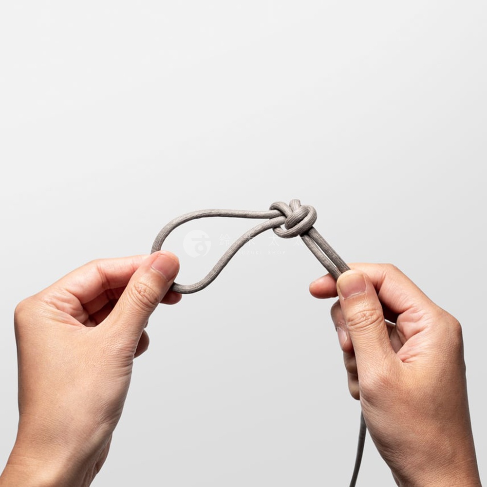 一雙手正抓住一條灰色編織繩，繩子打了一個結，形成一個繩圈。