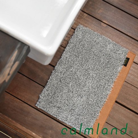 Ward Robe S 尺寸的灰色玄關地墊，材質為絨毛，觸感柔軟，背面有防滑設計，可放置於木質地板上，靠近一個白色陶瓷盆。