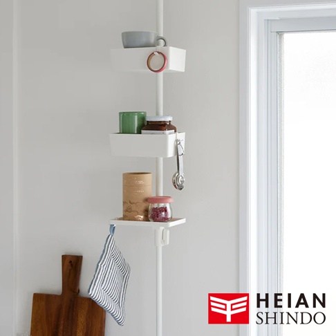 白色直撐架上層層堆疊著三個白色置物盒，分別裝有灰色杯子、綠色杯子、玻璃罐裝醬料、量匙、紙筒裝物品及紅色果醬小罐。置物盒下方掛著一條藍白條紋的布。