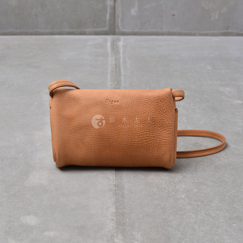 職人手作皮革Organ貼身斜背包，採用柔軟的淺棕色皮革製成，包身呈現簡潔的長方形輪廓，上方有細緻的品牌壓印，搭配一條細長的斜背帶，整體風格自然樸實。