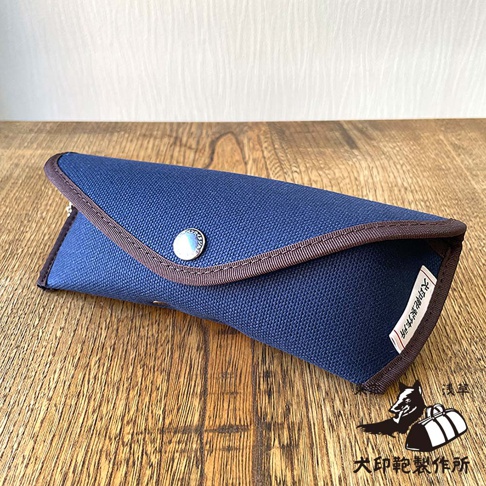 犬印鞄製作所的純綿帆布眼鏡收納盒，深藍色，帶有褐色滾邊和金屬鈕扣，右下角有品牌標誌和日文「淺草」字樣。