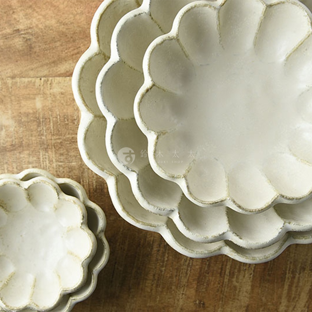 淺米色陶瓷碗盤堆疊，帶有花瓣狀邊緣，質感樸實，背景為木紋桌面。