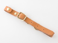 職人手作皮革背包用減壓胸前扣帶，採用 tan 色皮革製成，配有黃銅色針扣、鉚釘和 D 型環，用於調整和固定。