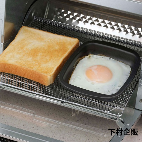 烤箱烤架上放置著一片金黃色吐司和一個黑色迷你方形烤盤，盤中煎著一個太陽蛋，蛋黃呈橘黃色，蛋白已凝固。