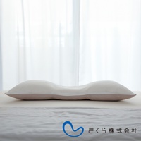 無敵低枕，白色網狀表層，內襯淺褐色布料，呈現S型曲線設計，置於白色床單上，後方為白色紗簾。