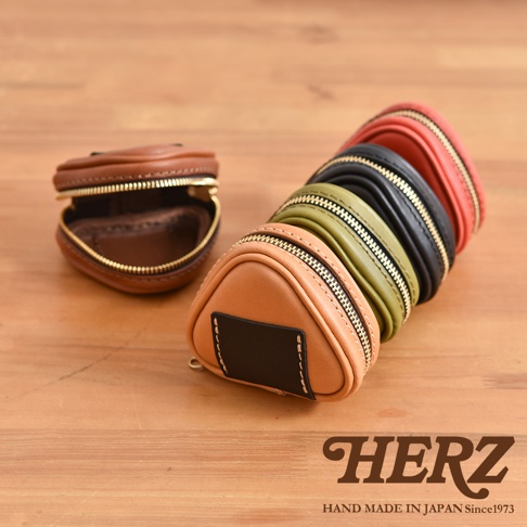 職人手作皮革三角飯糰造型小物收納包，共五色：棕色、駝色、軍綠色、黑色、紅色。採用光滑皮革材質，附有金色拉鍊，設計簡約實用。