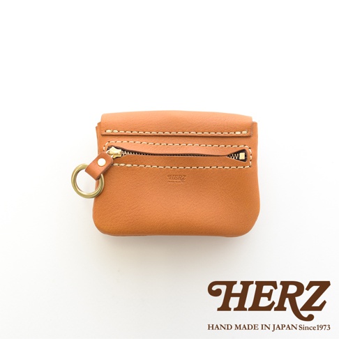 職人手作皮革旅行用雙層錢包，採用天然皮革材質，顏色為溫暖的棕褐色。錢包設有雙層設計，一個拉鍊開合，配有黃銅色金屬拉鍊和掛環，並壓印有「HERZ」品牌標誌。