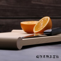 淺色木質砧板上放著對半切開的橘子和一把黑色手柄的刀，砧板右側邊緣圓潤，木紋清晰可見。