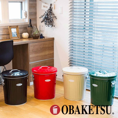 四個不同顏色的 OBAKETSU 垃圾桶，有黑色、紅色、米黃色和綠色，擺放在地板上，背景是百葉窗和木製櫃子。