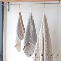 三條懸掛的 GRAPH 草木染格紋有機棉毛巾，淺米色、淺灰及米白色，格紋細緻，質感柔軟。