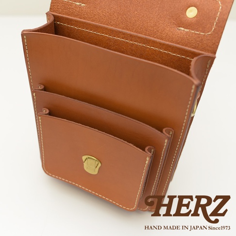 職人手作皮革單肩兩用小方包，採用鞣製的棕褐色皮革，車縫線清晰，設有翻蓋與金屬鎖扣，內部有夾層，展現簡約實用的設計。