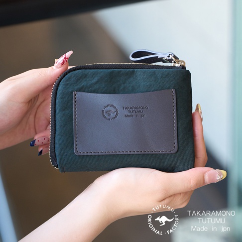 TUTUMU 品牌於深綠色防潑水迷你錢包上的皮革標籤，印有 TAKARAMONO TUTUMU Made in jpn 字樣，及一個袋鼠圖案。