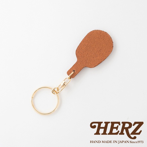 淺棕色皮革製成的桌球拍造型鑰匙圈，搭配金色金屬掛環與連接扣，展現職人手作質感。